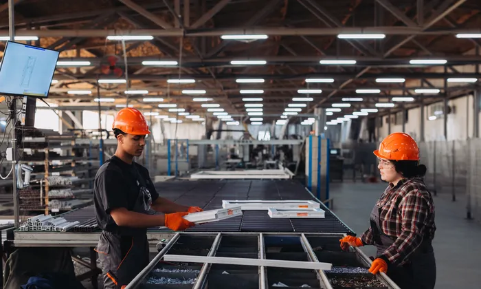 Two operators handling aluminium profiles by hand at an assembly bench in a window manufacturing plant