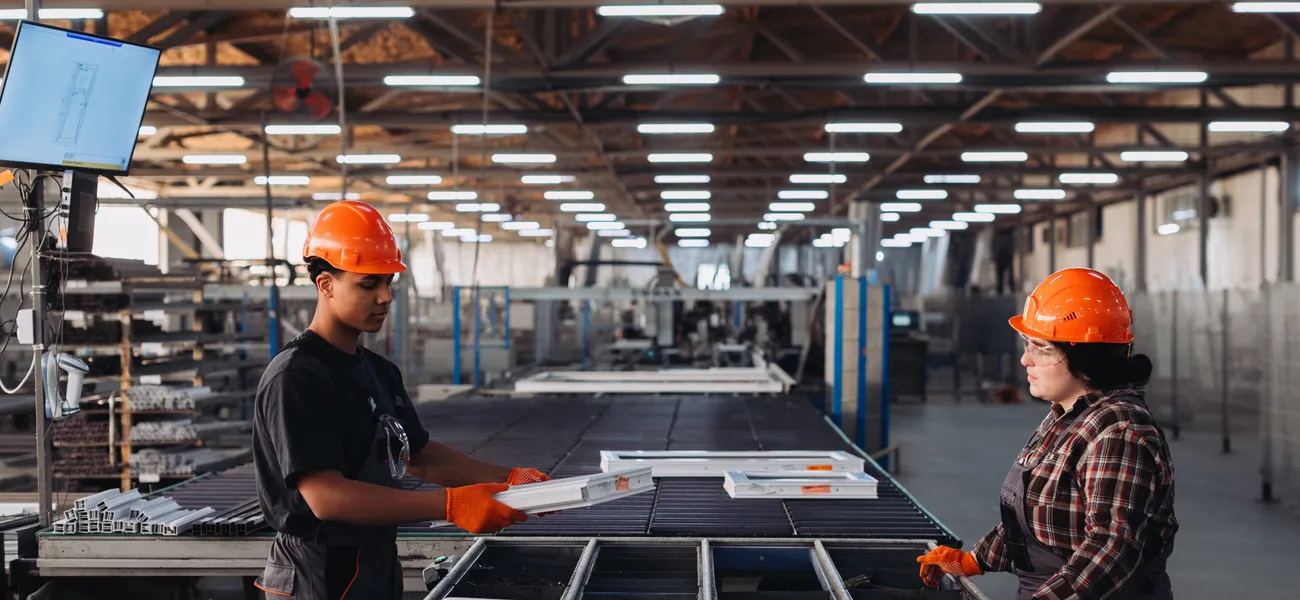 Two operators handling aluminium profiles by hand at an assembly bench in a window manufacturing plant